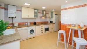 A compact kitchen with a washing machine, a microwave, and a small dining area with stools. - Villa Morret Moraira by Cabrera Homes (Teulada)