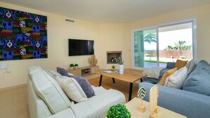 A living room with a sofa, a coffee table, a flat-screen TV, a fireplace, and a large window. - Villa Morret Moraira by Cabrera Homes (Teulada)