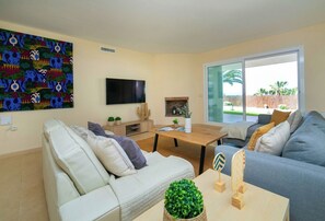 Ein Wohnzimmer mit einer Couch, einem Couchtisch, einem Flachbildfernseher, einem Kamin und einem großen Fenster.