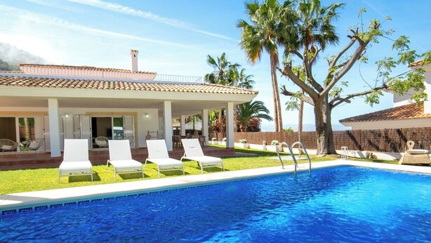A pool with lounge chairs, a covered patio, and palm trees. - Villa Morret Moraira by Cabrera Homes (Teulada)
