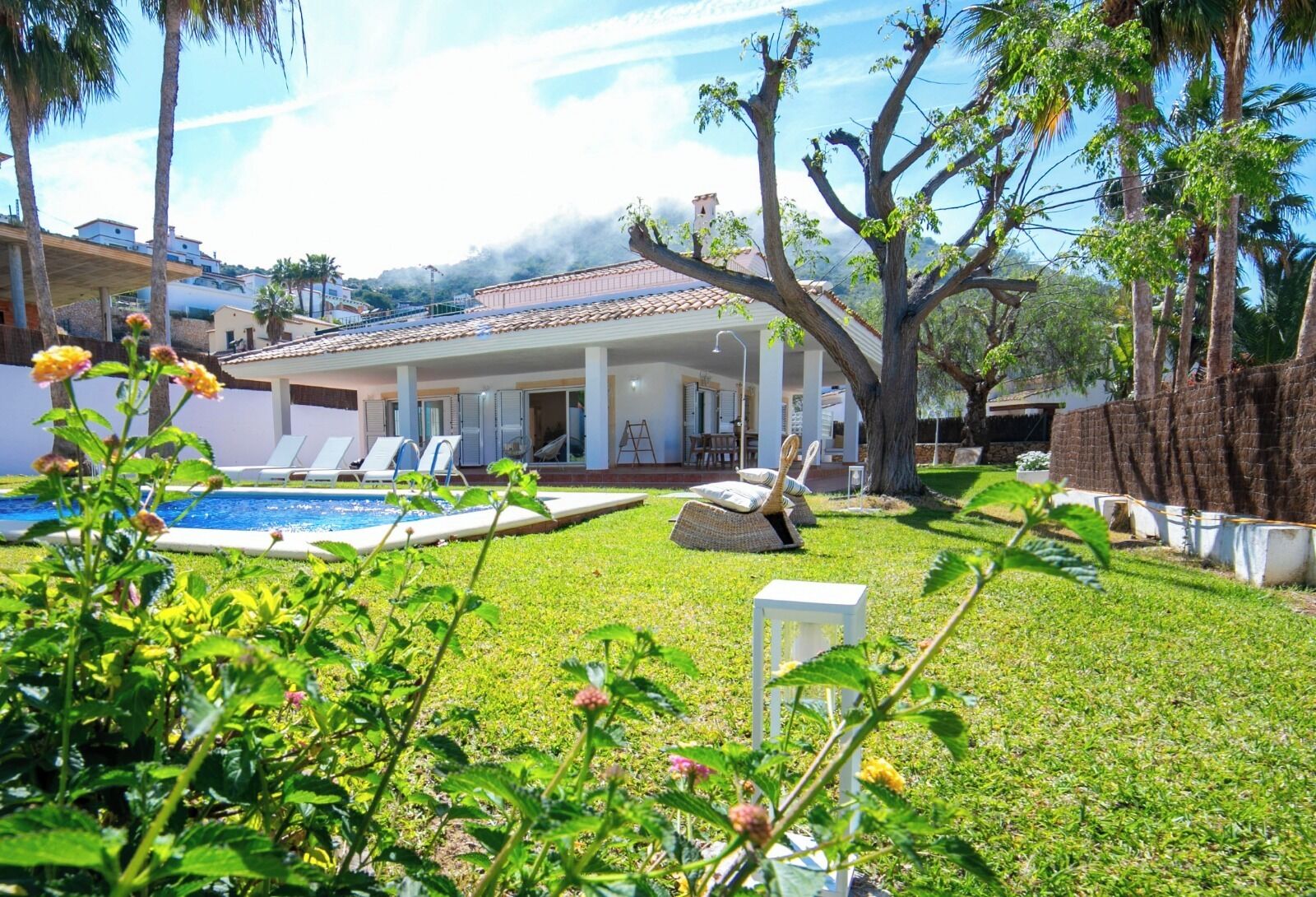 A pool area with lounge chairs, a covered patio, and a view of a mountain.