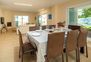 A dining area with a table set for four, chairs, a sofa, a TV, and a fireplace.