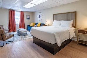Una habitación de hotel con cama, escritorio, silla, sofá y ventana con cortinas.