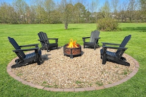 Un espacio de asiento al aire libre con forma circular, con cuatro sillas Adirondack alrededor de un brasero central.