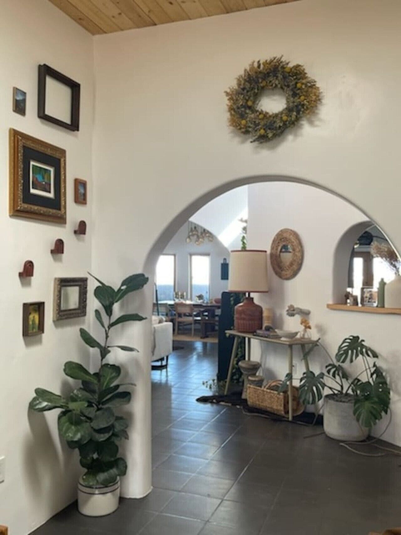 A room with a large arched doorway, a potted plant, a wall-mounted mirror, and a shelf with decorative items.