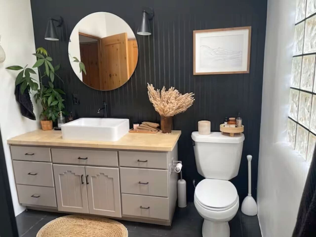 A bathroom with a sink, toilet, mirror, and a framed picture on the wall.
