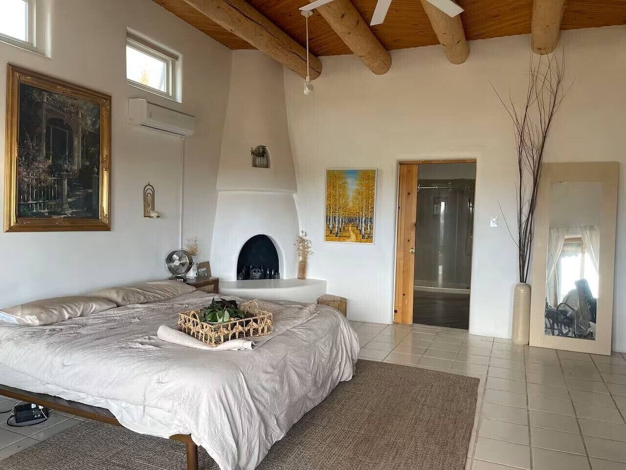 A bedroom with a bed, a fireplace, a painting, and a mirror.
