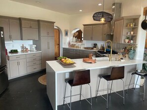 A modern kitchen with a central island, bar stools, and a variety of appliances and decor. - Casa Encantado in Eldorado (Santa Fe)