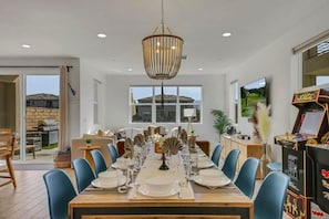A dining area with a long table set for a meal, a chandelier, and a video game machine. - Sunset by the Lake | Heated Pool, Spa & Arcade (Indio)
