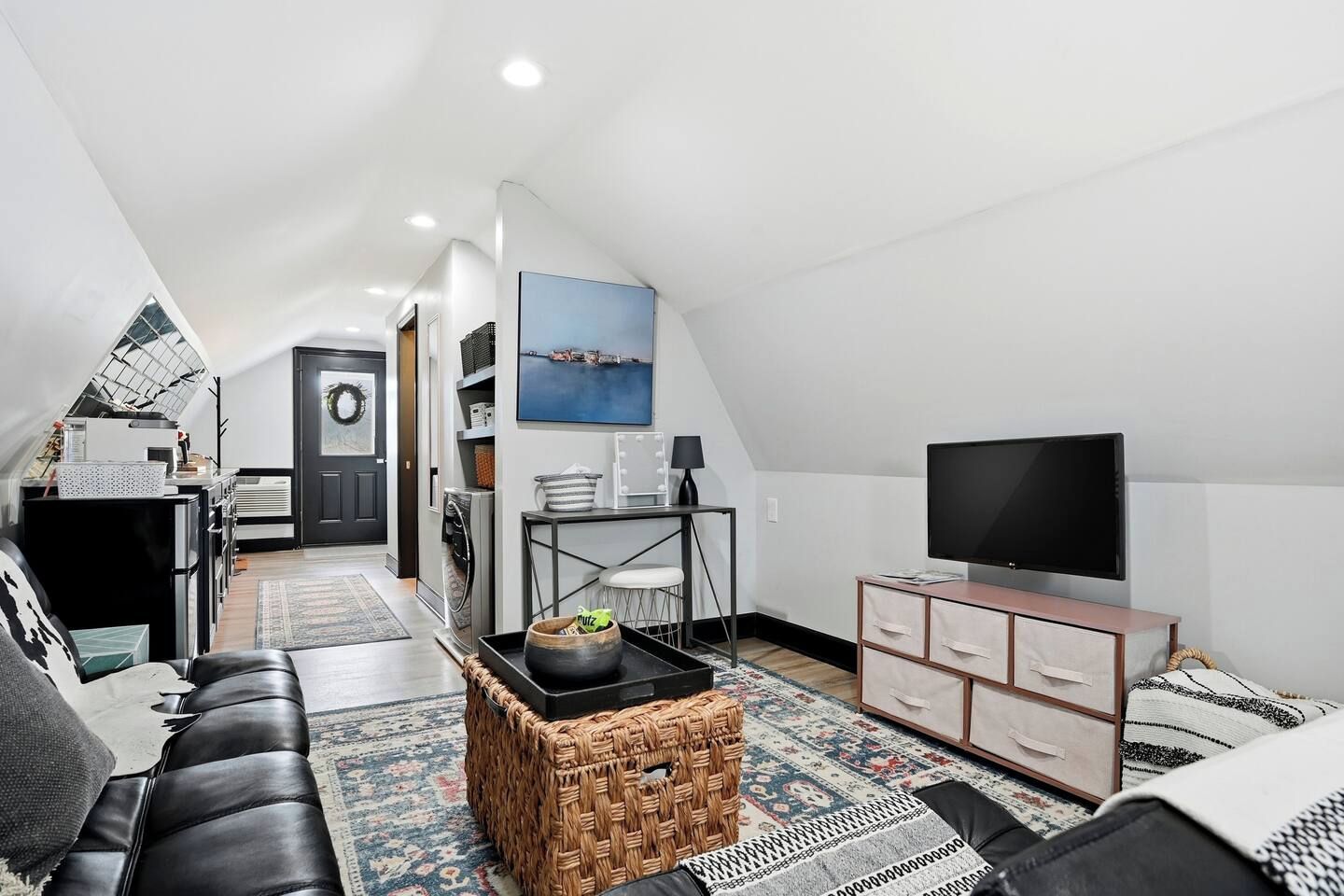 A modern loft apartment with a high ceiling, a television, a dining area, and a kitchen.