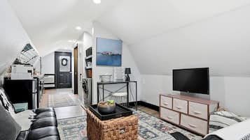 A modern loft apartment with a high ceiling, a television, a dining area, and a kitchen.