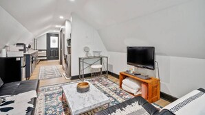 A compact, well-lit attic room with a kitchenette, a TV, a sofa, and a patterned rug. - Romantic Barn Loft | Wine Country & Weddings (Paeonian Springs)