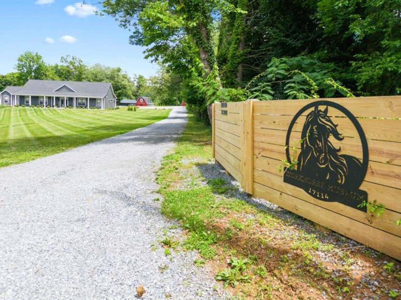 A gravel driveway leading to a building with a wooden fence and a horse logo.
