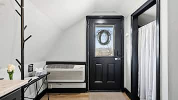 Een kamer met een zwarte deur, een witte airconditioner, een klein tafeltje met een bloevas en een kapstok.
