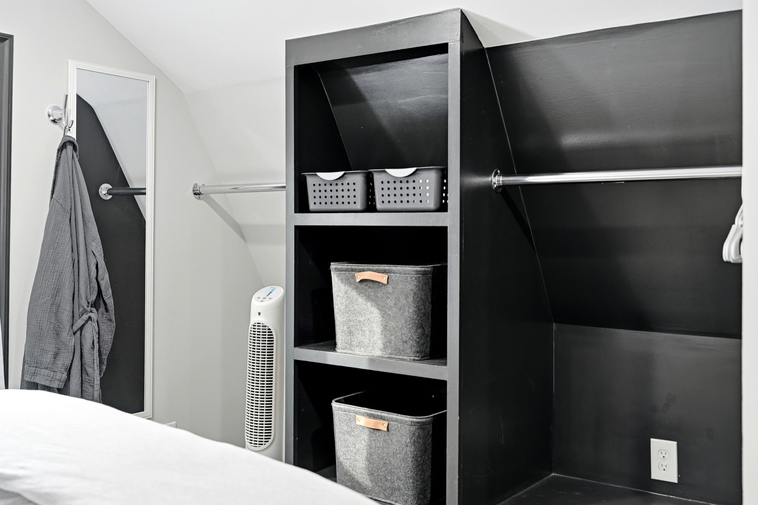 A modern bedroom with a bed, a wardrobe, and built-in storage with baskets and bins.
