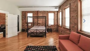 Una camera da letto con un letto a baldacchino, una ventola a soffitto, pareti in mattoni e ampie finestre.