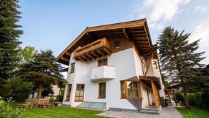 Una casa a due piani con un balcone in legno, vialetto in pietra e prato curato.