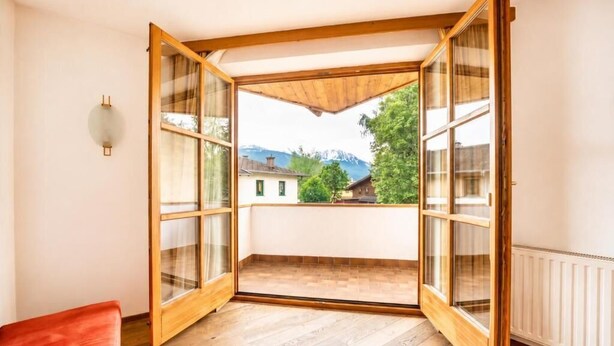 Una stanza con pavimento in legno, una panca rossa e vista su montagne e alberi attraverso ampie vetrate.