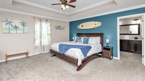 Een slaapkamer met een bed, een bankje, een plafondventilator, een surfboard decoratie en uitzicht op de badkamer.
