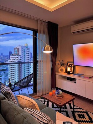 Ein modernes Wohnzimmer mit großem Fenster, einer Couch, einem Couchtisch, einem Fernseher und einem Balkon.