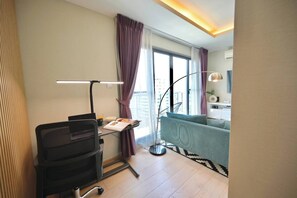 Ein modernes Wohnzimmer mit Schreibtisch, Stehlampe, Sofa und einem großen Fenster mit Vorhängen.
