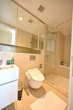 A modern bathroom with a glass shower enclosure, a white toilet, and a sink with a mirror above it. - 5 min Metro| KingBed | Kitchen full | Netflix WiFi (Watthana)