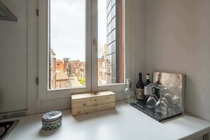 A kitchen with a window, a wooden box, a glass container, and wine bottles. - Historic Dorsoduro Apartment with Balcony Near Guggenheim & Zattere (Venezia)