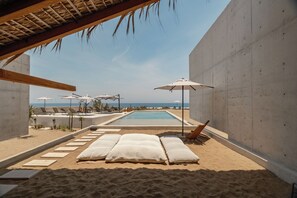 Ein Poolbereich direkt am Strand mit Liegestühlen, Sonnenschirmen und Blick auf das Meer.