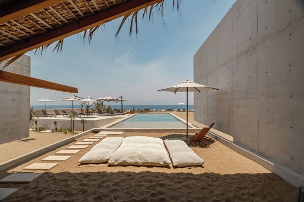 A beachside pool area with lounge chairs, umbrellas, and a view of the ocean. - Casa Talá by Lumina (Santa María Colotepec)