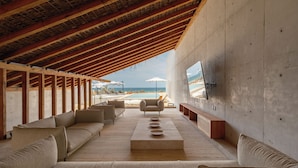 An open-plan living area with a wooden ceiling, a large sofa, a coffee table, and a TV mounted on the wall. - Casa Talá by Lumina (Santa María Colotepec)