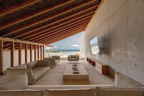 An open-plan living area with a wooden ceiling, a large sofa, a coffee table, and a TV mounted on the wall. - Casa Talá by Lumina (Santa María Colotepec)