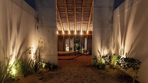 A covered outdoor area with a sandy floor, concrete walls, and a thatched roof structure. - Casa Talá by Lumina (Santa María Colotepec)