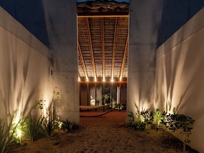 A covered outdoor area with a sandy floor, concrete walls, and a thatched roof structure. - Casa Talá by Lumina (Santa María Colotepec)