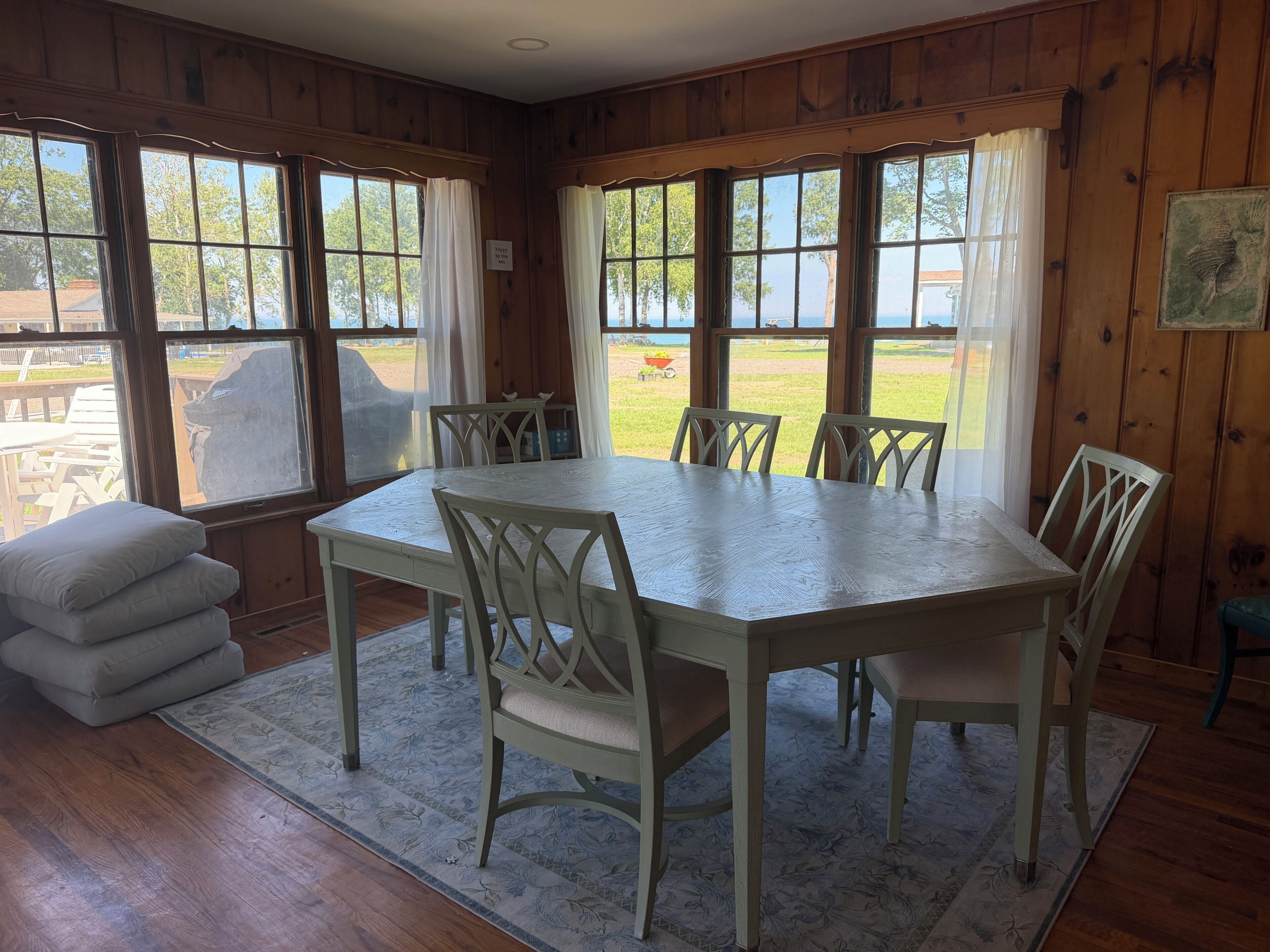 Une salle à manger avec une grande table et des chaises, des murs lambrés et de grandes fenêtres avec des rideaux.