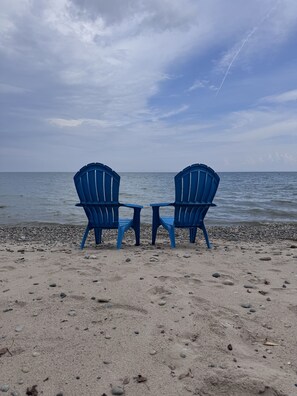 Two blue chairs facing the sea on a pebbly beach.
