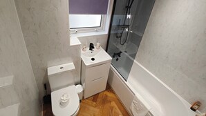 Une petite salle de bain comprenant des toilettes, un lavabo et une douche fermée par une paroi de verre.