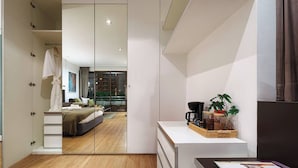 Un dormitorio moderno con un espejo grande, una cama, una cafetera y una planta pequeña sobre un tocador blanco.