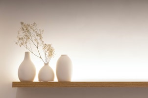 Three white vases on a wooden shelf against a plain wall.