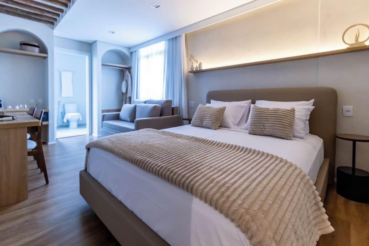 Quarto de hotel moderno com cama grande, escrivaninha e vista para o exterior.
