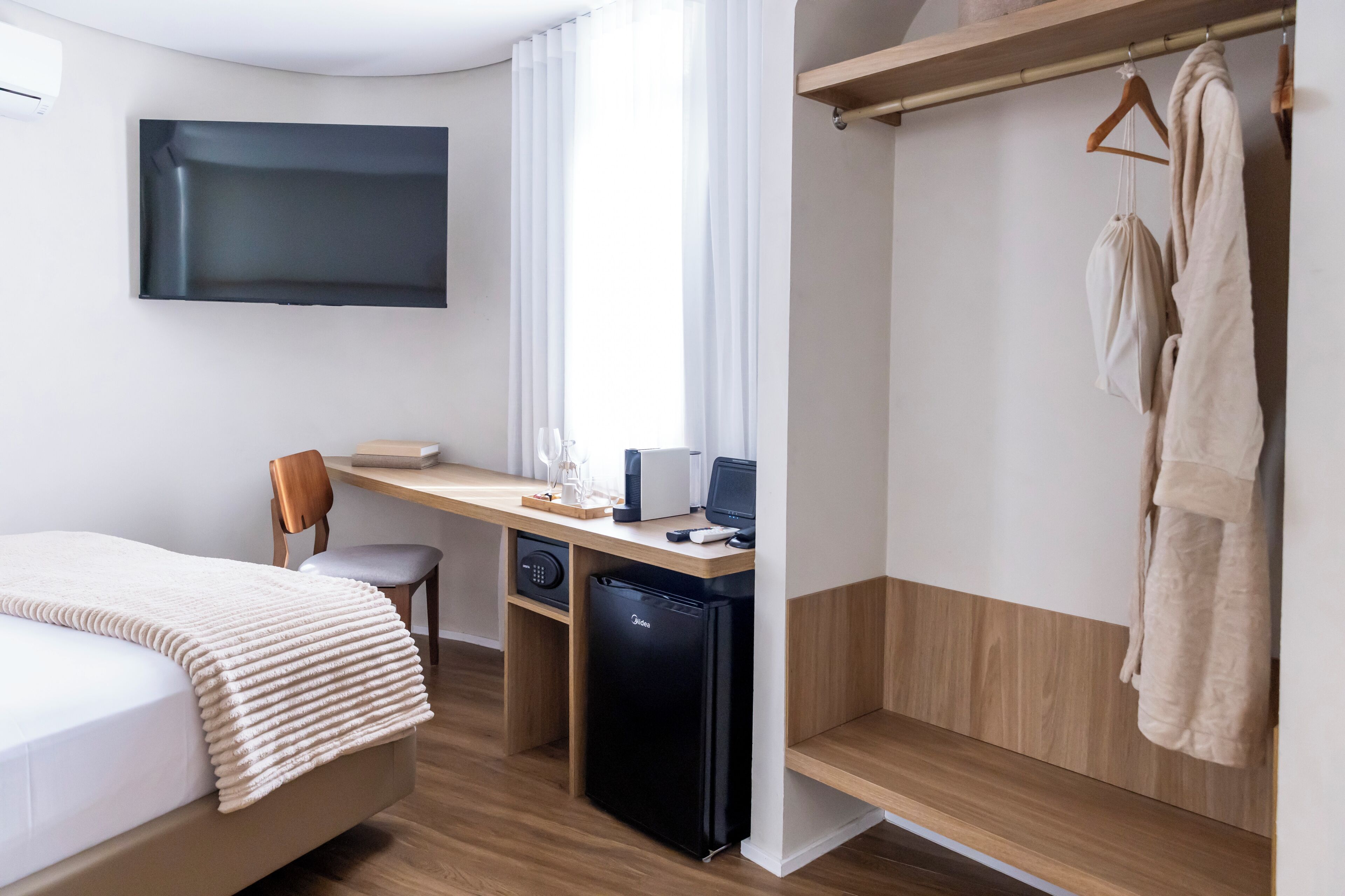 Habitación de hotel con cama, escritorio, silla, televisión y armario.