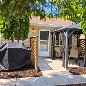 A covered patio area with outdoor furniture, a grill, and a door leading to a house. - The Mermaid (Wasaga Beach)
