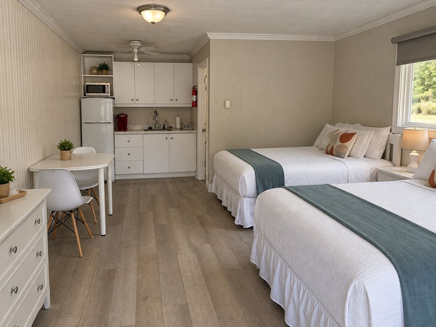 A compact room with a kitchenette, two beds, a desk, and a chair.