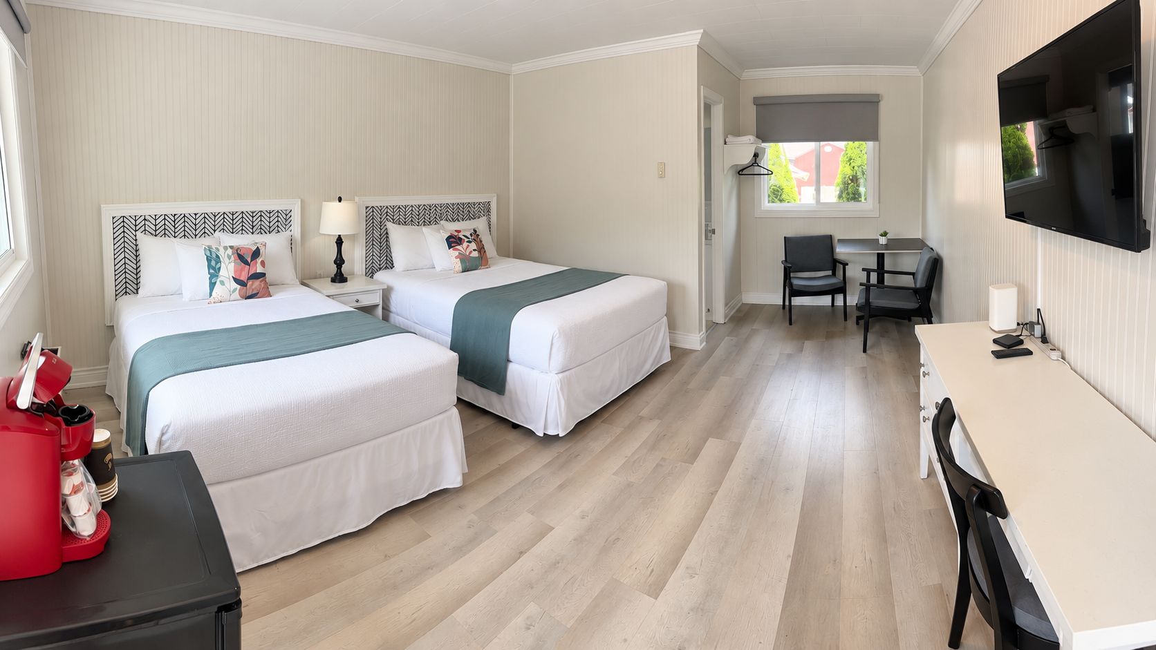 A hotel room with two beds, a desk, a chair, a TV, and a window.