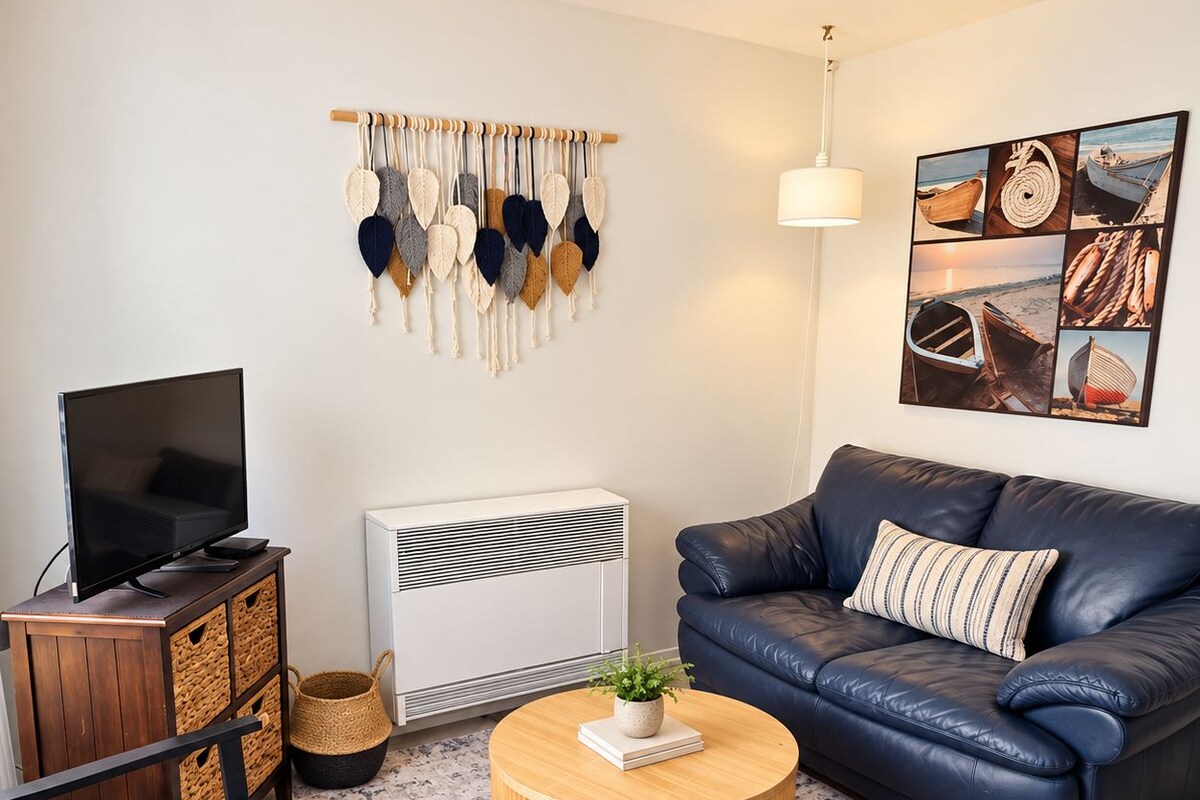 A modern living room with a leather sofa, a flat-screen TV, a round wooden coffee table, and a wall-mounted macrame piece.