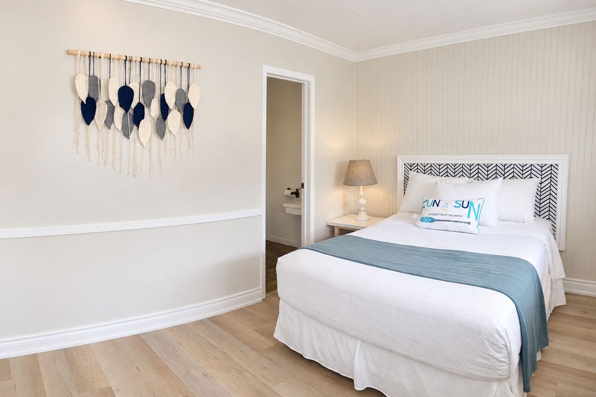A hotel room with a bed, bedside table, lamp, and a wall decoration.