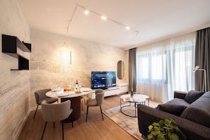 A modern living room with a dining area, a flat-screen TV, and a large window with curtains.