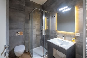 A modern bathroom with a glass-enclosed shower, a white toilet, and a vanity with a mirror. - Boutique Suites (Lugano)