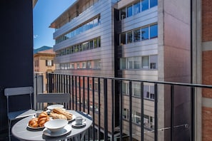 A balcony with a table set for breakfast, including croissants and coffee, overlooking a modern building with multiple windows. - Boutique Suites (Lugano)