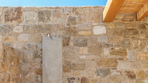 A stone wall with a wooden door and two white vases with handles. - Vendema Residence Mykonos (Mikonos)
