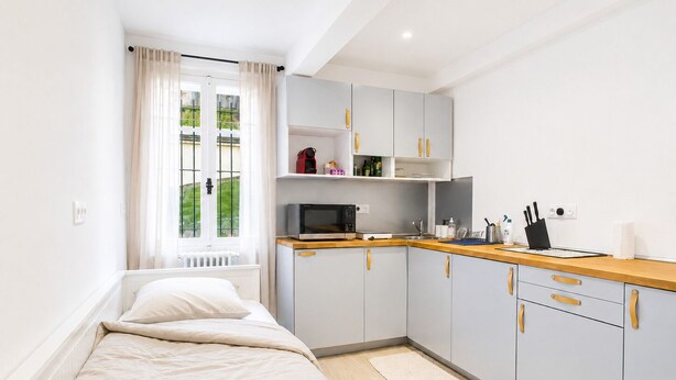 Quarto compacto com cama, espaço de cozinha compacto e janela com cortinas.